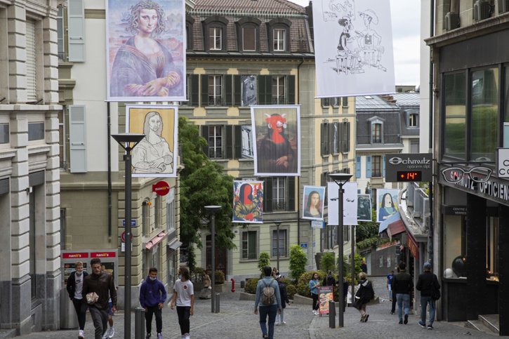 Des personnes passent sous les images monumentales de l'exposition "Mona Lôzane", déployées dans les rues de Lausanne. © Keystone/SALVATORE DI NOLFI