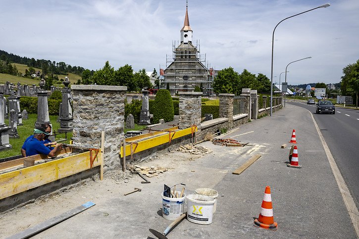 Des ouvriers reconstruisent le mur du cimetière, à côté du Temple des Eplatures qui vient de retrouver son clocher, qui avait été balayé par la tempête. © Keystone/JEAN-CHRISTOPHE BOTT